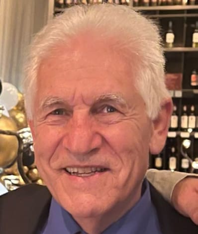 A man with white hair and blue shirt smiling.
