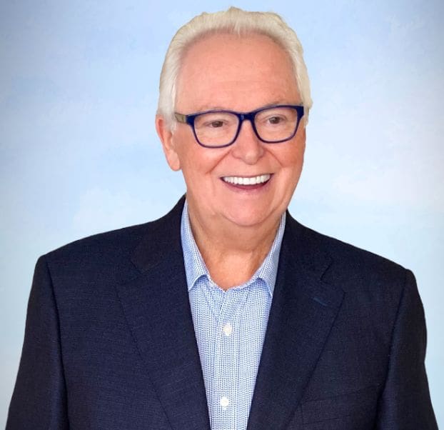 A man with white hair and glasses smiling.